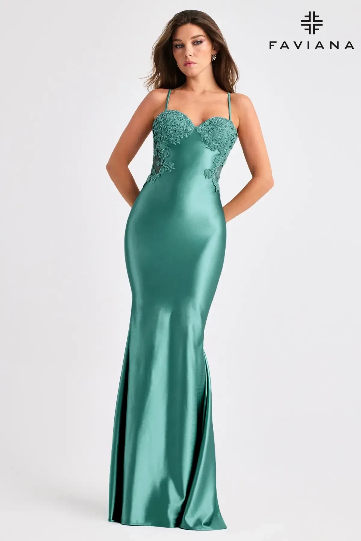 A woman wearing a form-fitting, teal satin gown with thin straps and floral embroidery at the bodice.