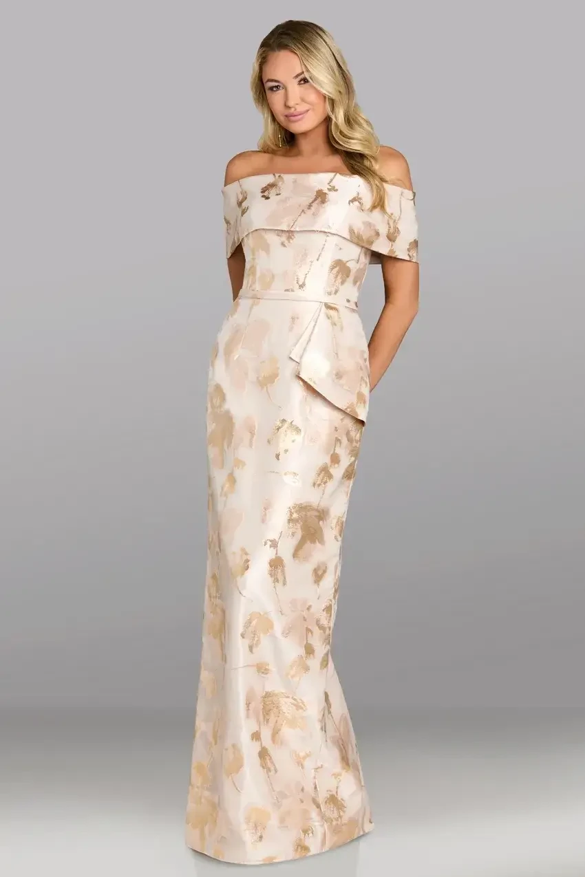 A woman wearing a form-fitting, off-the-shoulder gown with a floral pattern and a side pocket, standing against a gray background.
