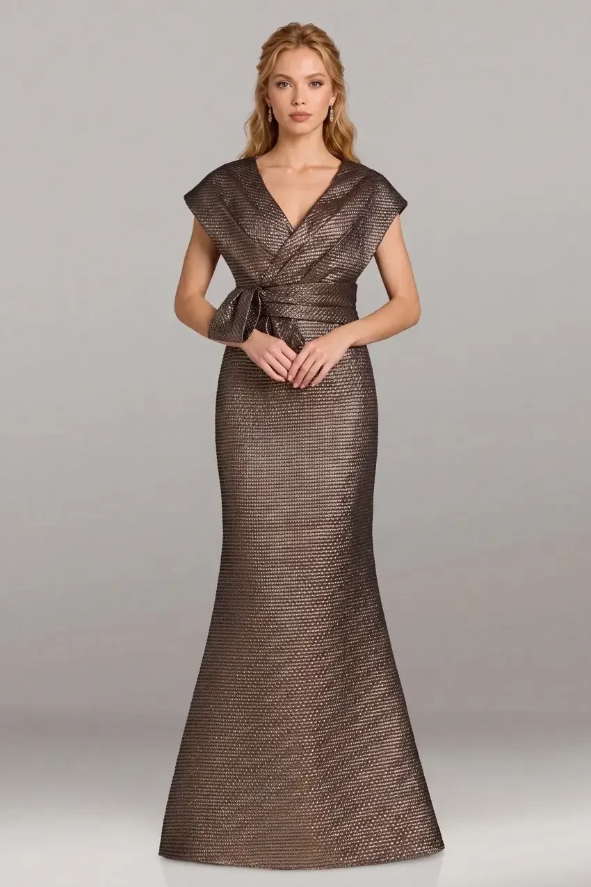 A model wearing a stylish bronze gown with a fitted mermaid silhouette and a wrap design, featuring cap sleeves and a belt detail.