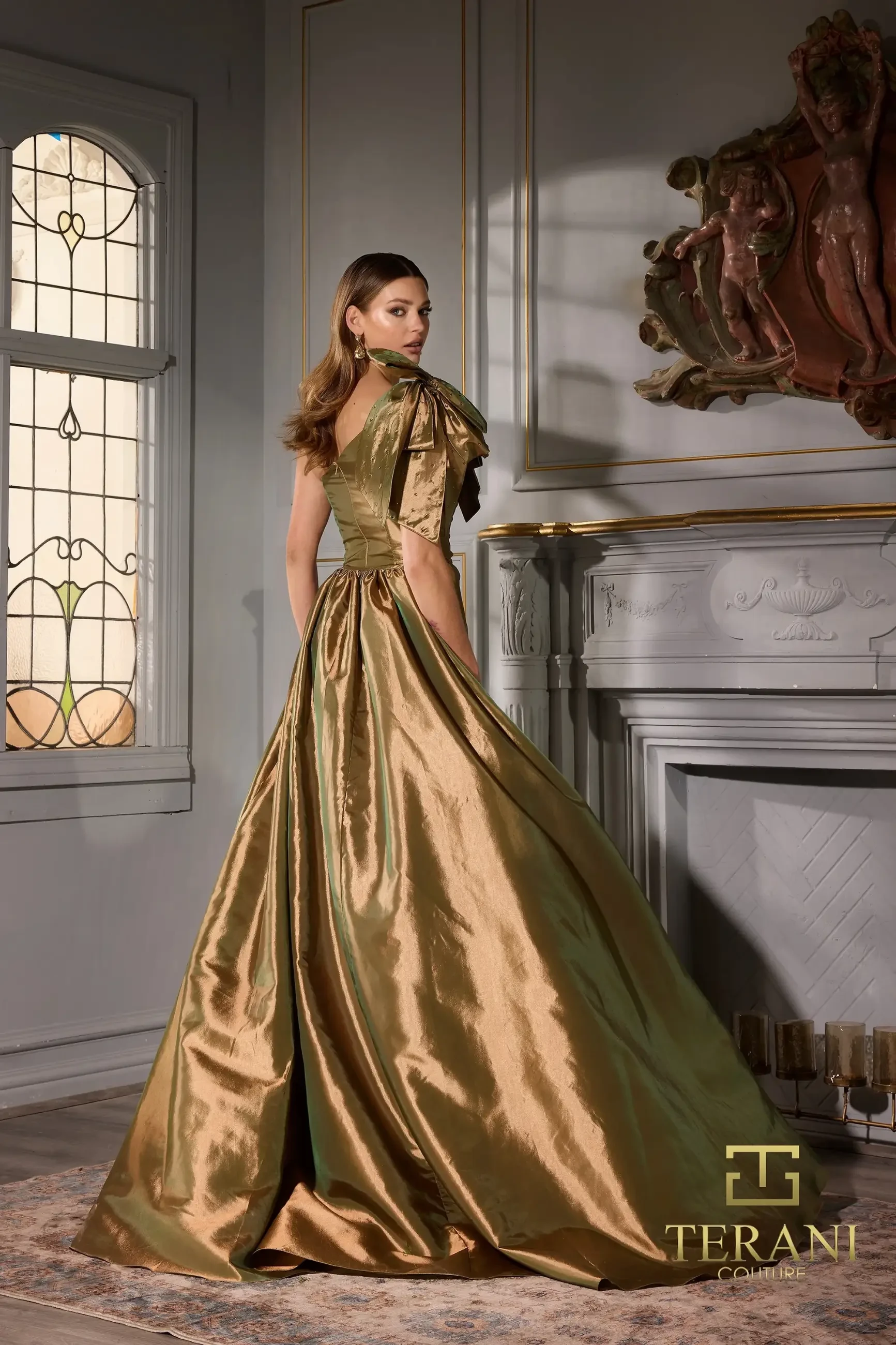 Model is wearing the Terani 252E5531, a radiant gold high-slit sleeveless gown with an asymmetric neckline, one-shoulder cap sleeve, and luxurious stretch taffeta.