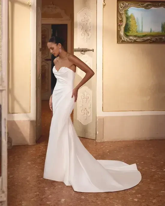 Model is wearing a stretch Mikado fit-and-flare wedding gown with a peek-a-boo sweetheart neckline, beading, sequins, and lace detailing.