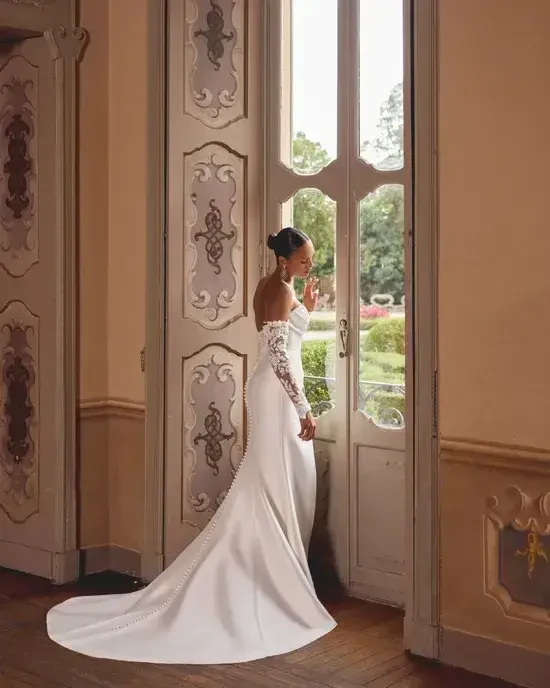 Model is wearing a stretch Mikado fit-and-flare wedding gown with a peek-a-boo sweetheart neckline, beading, sequins, and lace detailing.