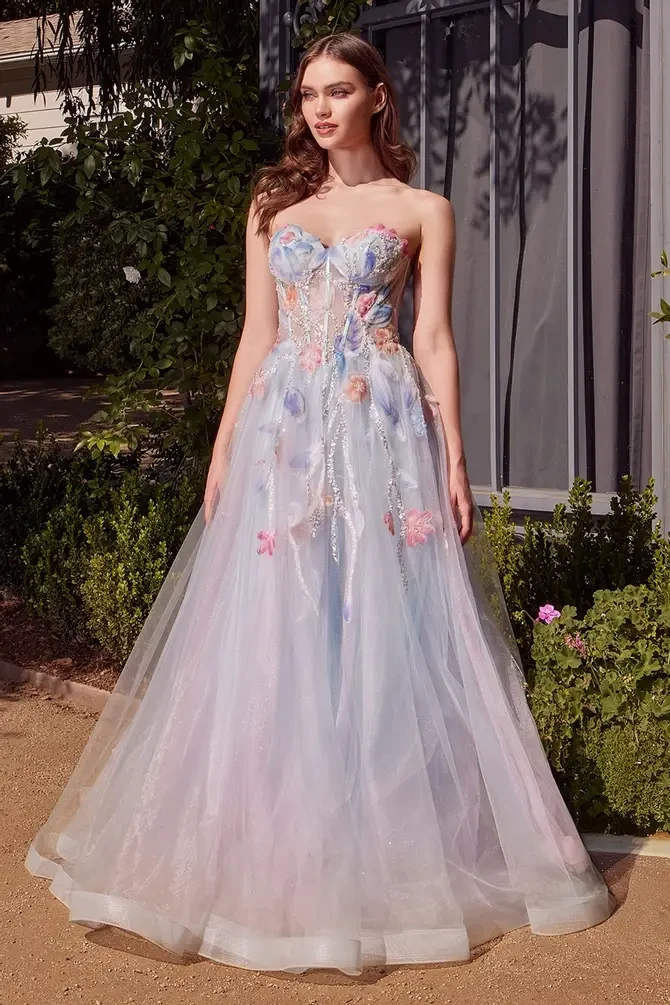 Model is wearing a strapless ball gown with a sweetheart neckline, sheer bodice, watercolor floral appliqués, soft tulle layers, and light beading.