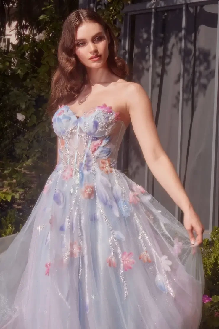 Model is wearing a strapless ball gown with a sweetheart neckline, sheer bodice, watercolor floral appliqués, soft tulle layers, and light beading.