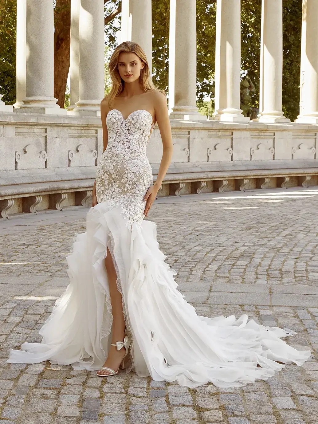 Model is wearing a mermaid bridal gown with a high sweetheart neckline and pleated tulle and organza ruffles on the skirt 