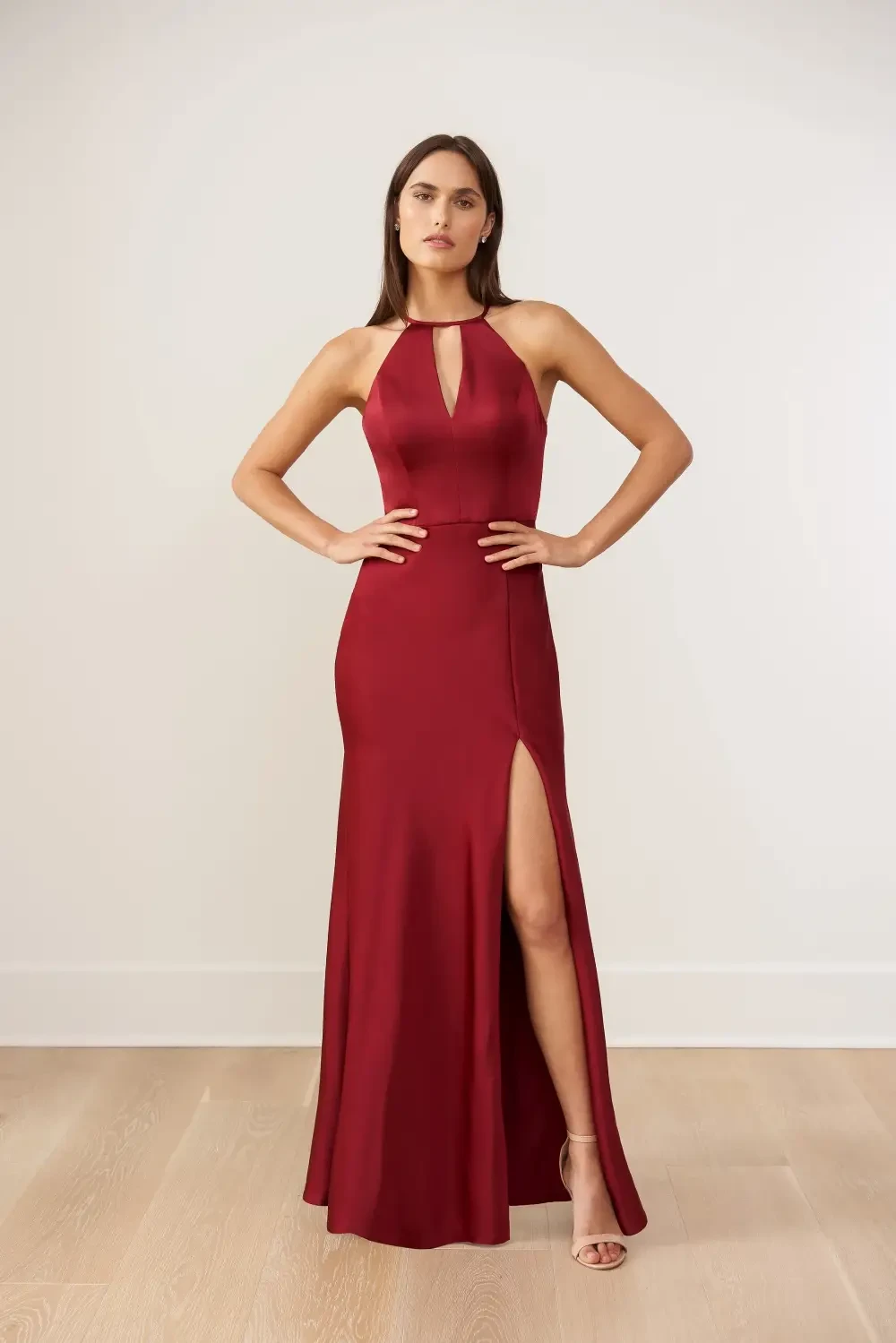 A model wearing a burgundy evening gown with a high slit and a halter neckline, striking a pose against a neutral background.