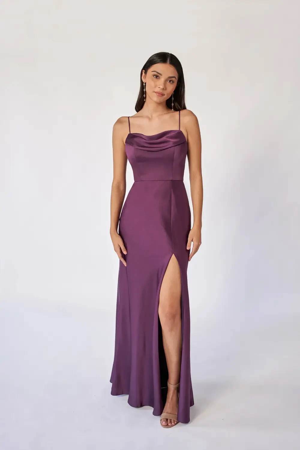 A woman wearing a purple evening dress with a thigh-high slit, posing against a plain background.