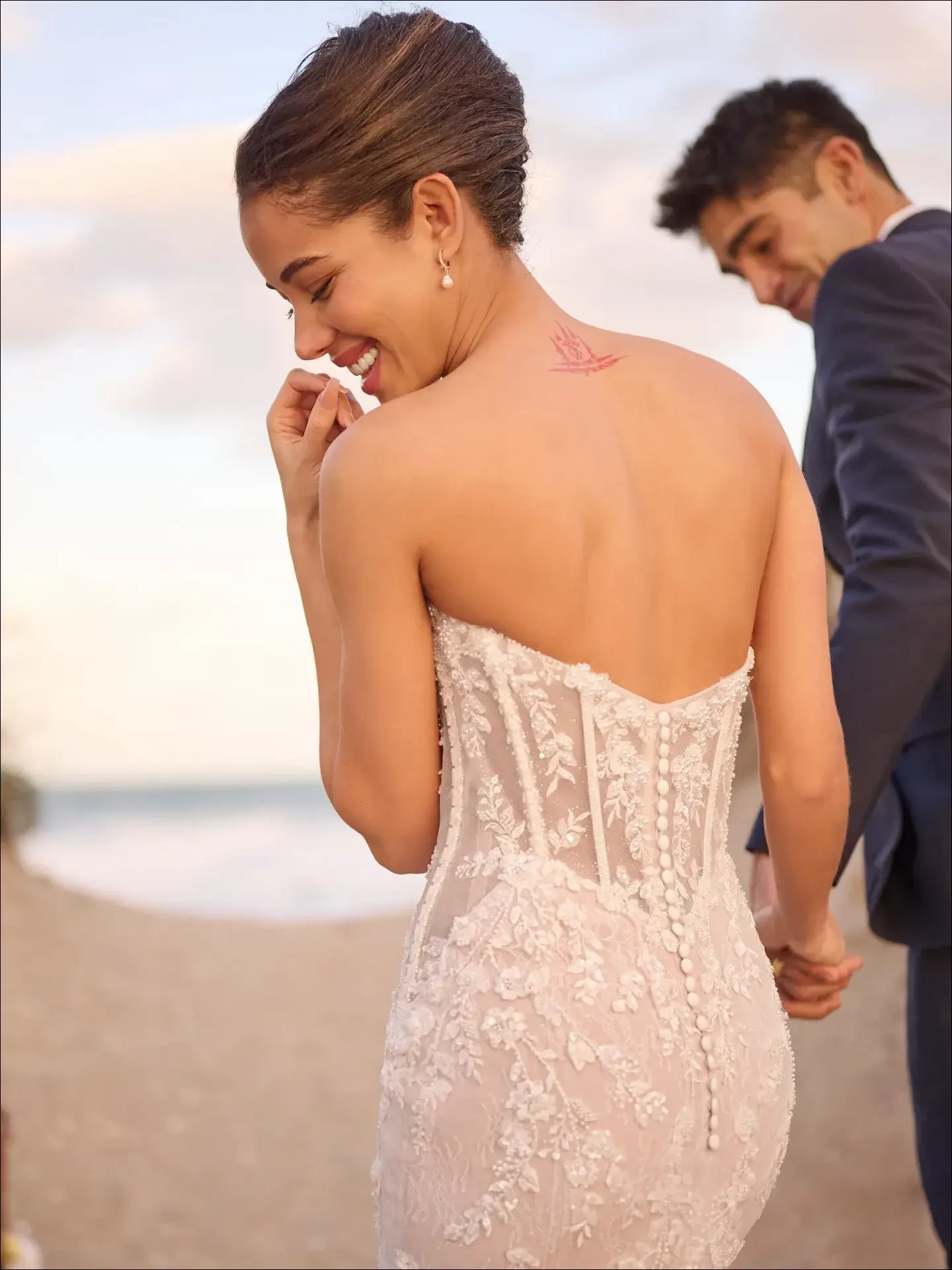 Model is wearing a strapless mermaid gown with shimmering beaded details and a dramatic, curve-hugging silhouette.