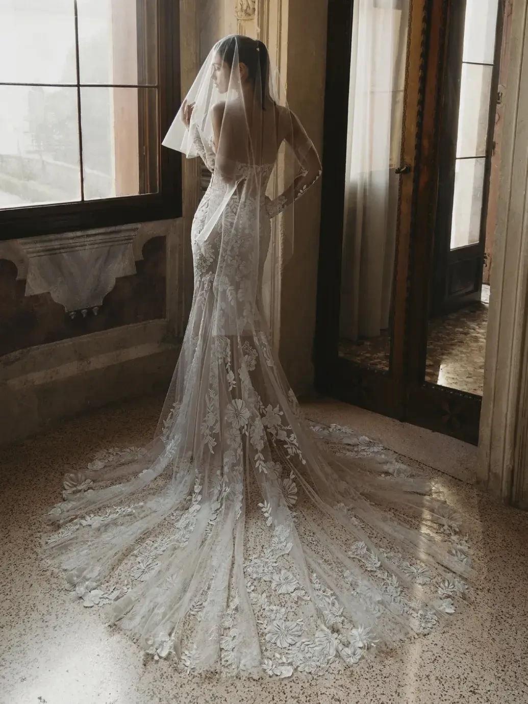 Model is wearing a sleek sheath wedding gown with 3D crepe floral embroidered lace over soft tulle and chiffon for an elegant, lightweight look.
