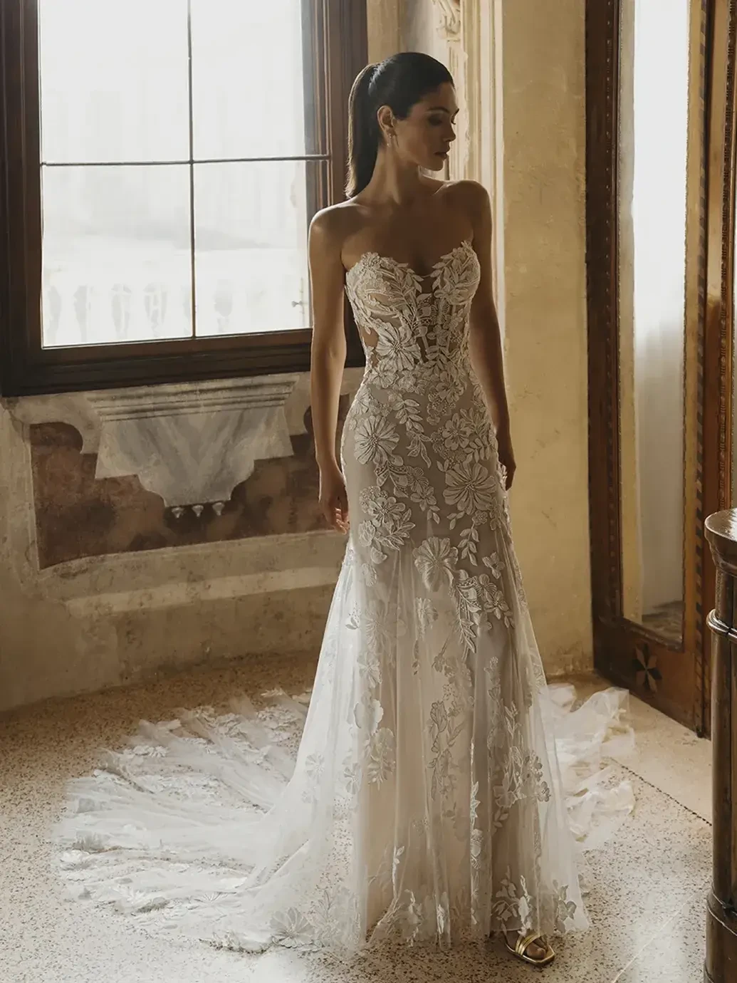 Model is wearing a sleek sheath wedding gown with 3D crepe floral embroidered lace over soft tulle and chiffon for an elegant, lightweight look.