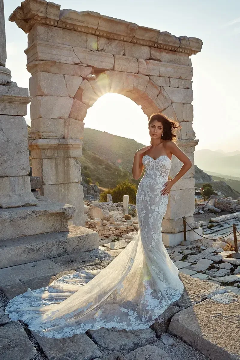 Model is wearing a strapless fit-and-flare wedding gown with a soft sweetheart neckline, champagne-skin illusion bodice, ivory lace, sequins, and Chantilly lace layers.