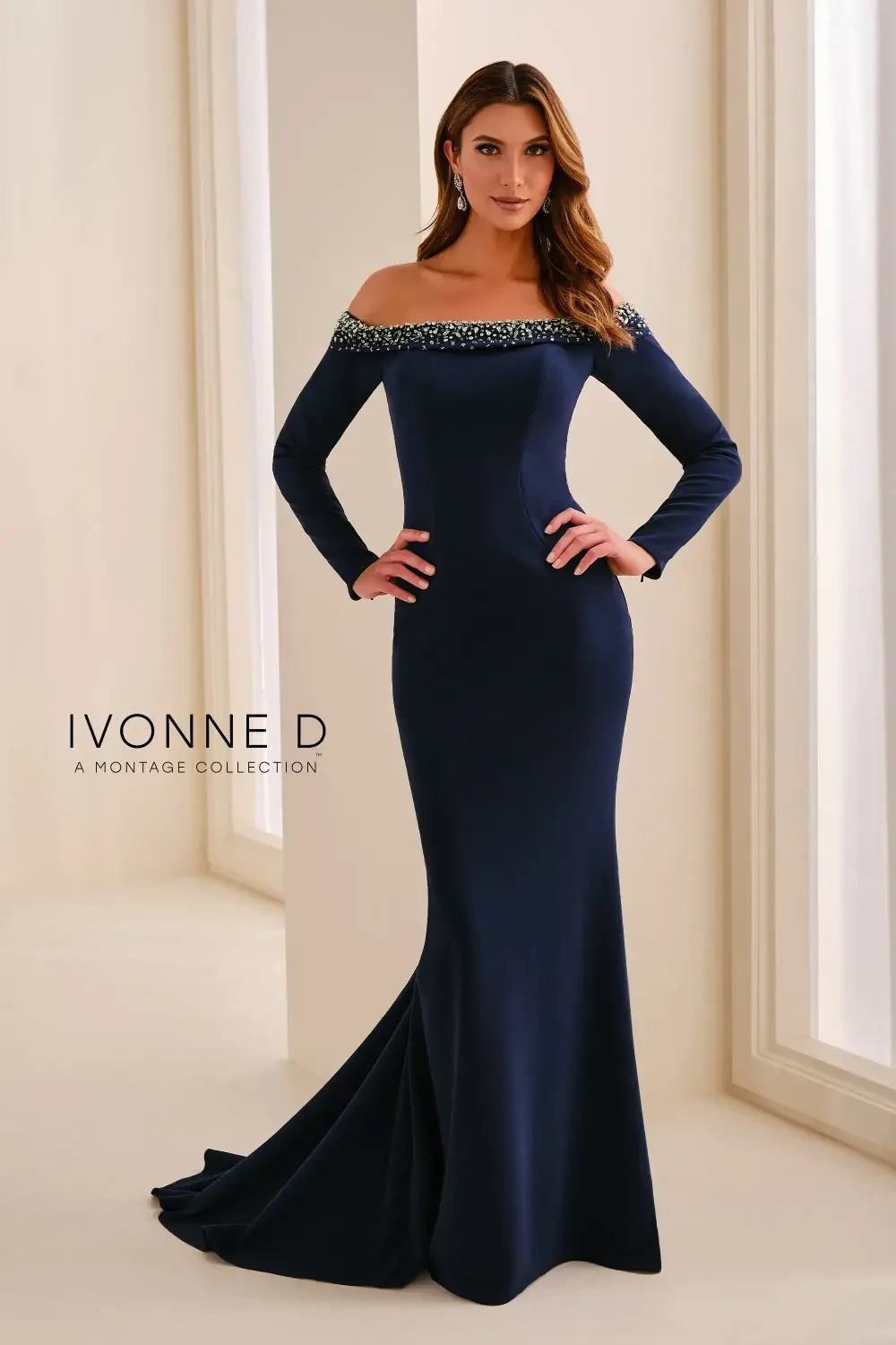 A model wearing a navy blue off-the-shoulder gown with embellishments, standing elegantly in a well-lit room.