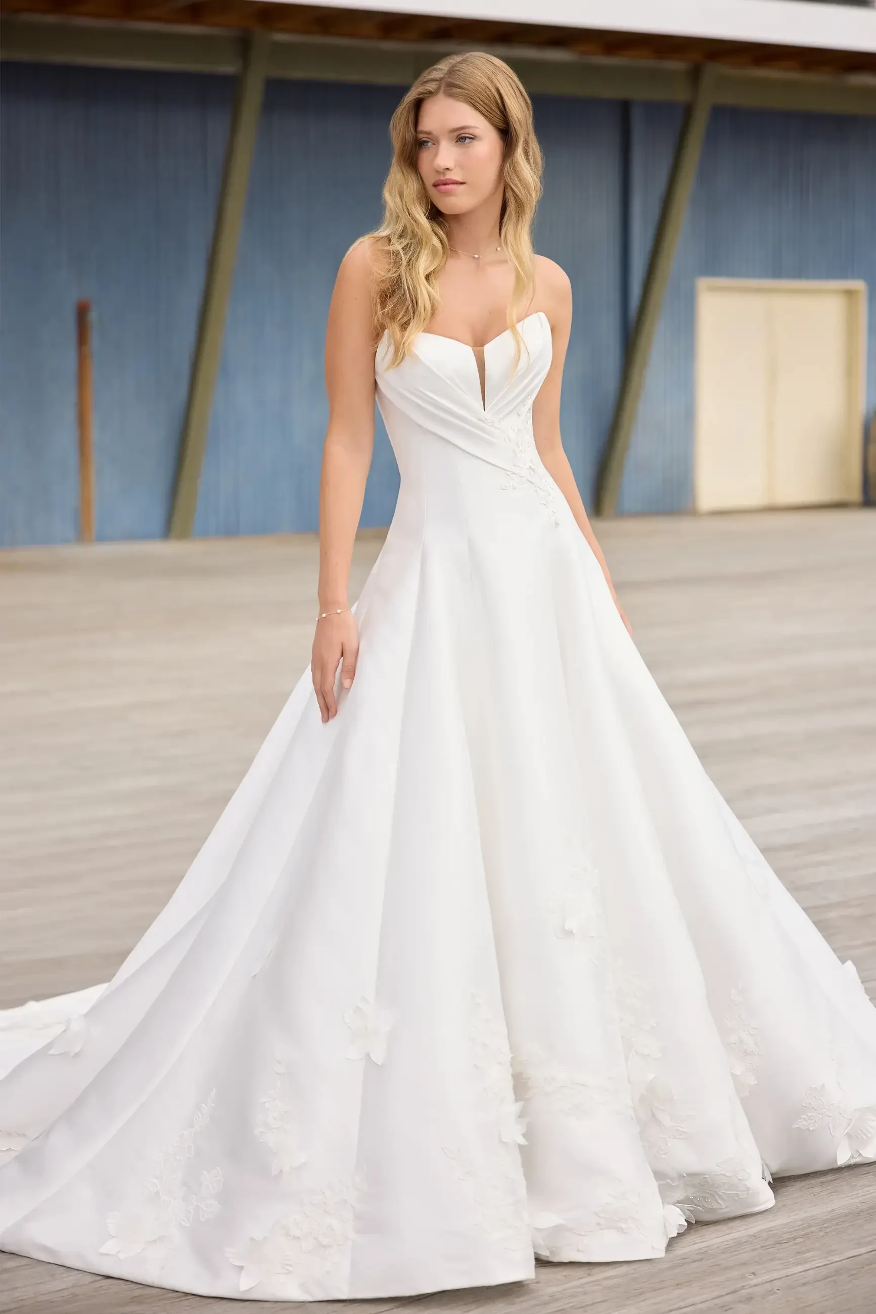 Model is wearing a strapless ball gown with a sweetheart neckline, draped bodice, and 3D floral appliques for timeless sophistication.
