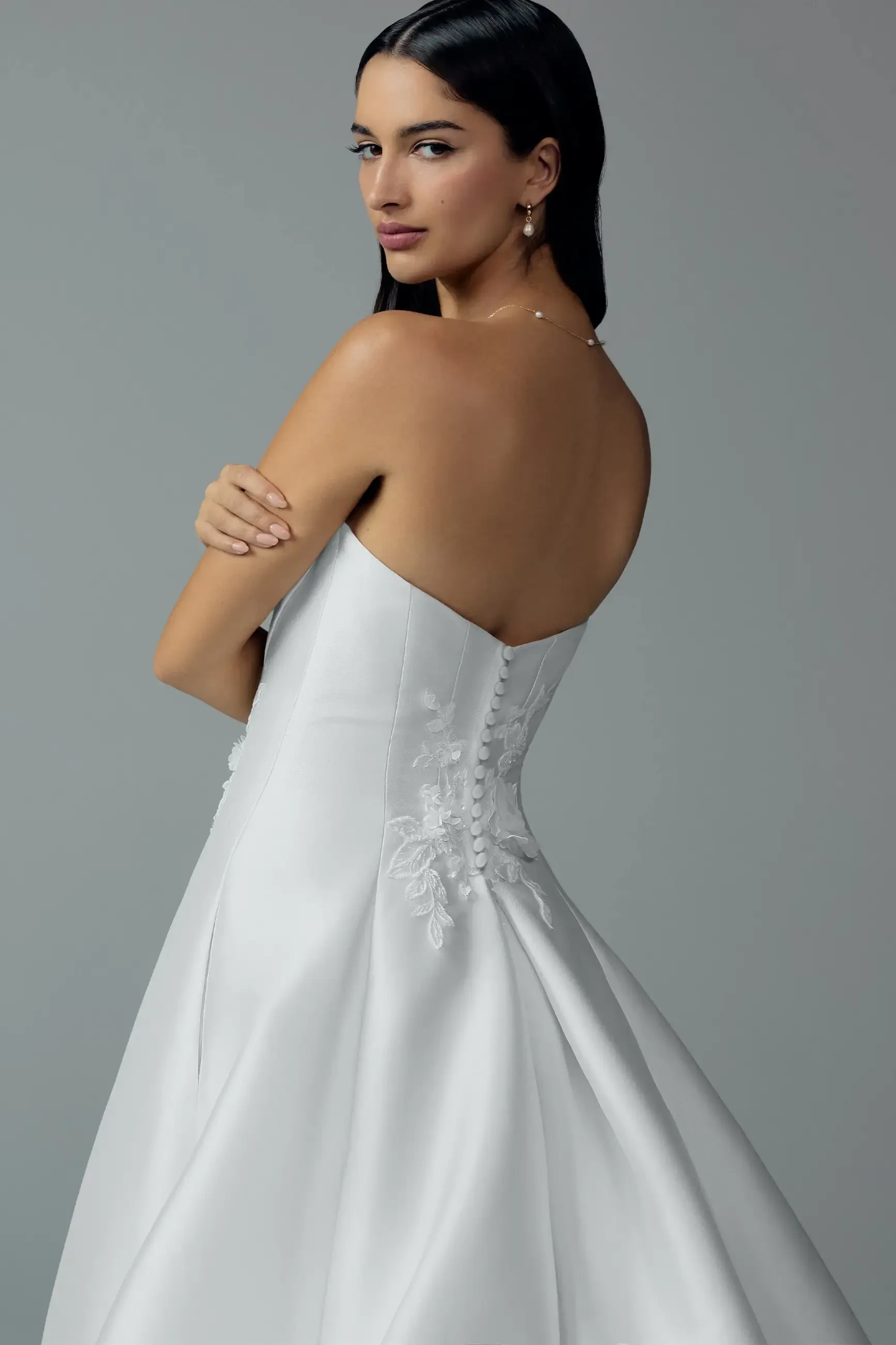 Model is wearing a strapless ball gown with a sweetheart neckline, draped bodice, and 3D floral appliques for timeless sophistication.