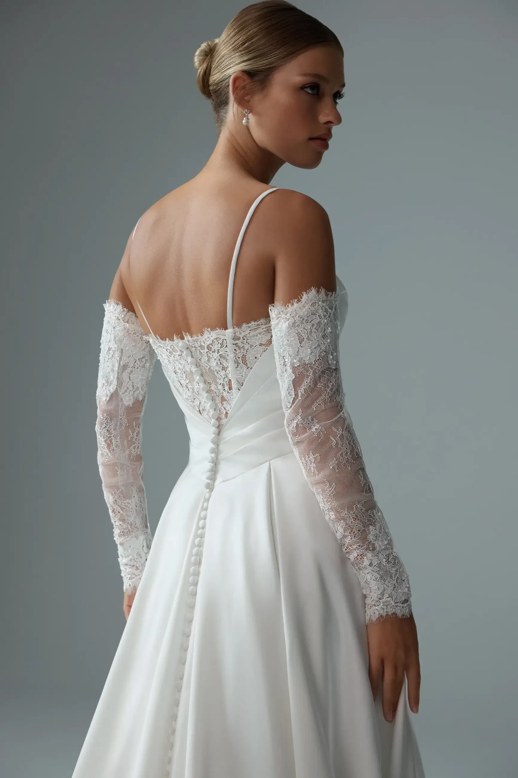 Model is wearing a luxurious satin gown with a delicately ruched bodice, off-the-shoulder lace sleeves, and spaghetti straps for a modern romantic look.